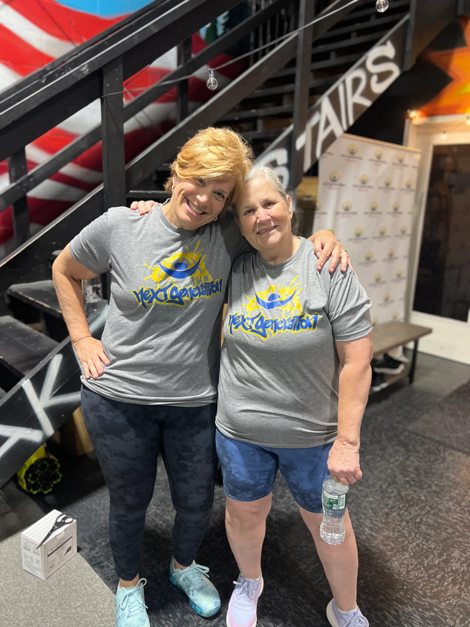 Two women in Next Generation shirts smiling at the gym